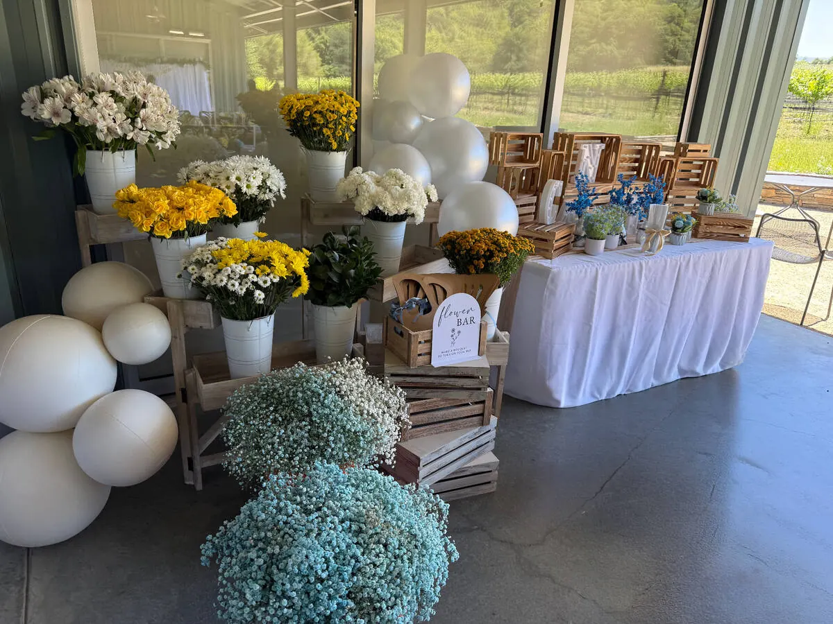 Bloom bar stocked with yellow roses, daisies and baby's breath beside ribbon and wrapping for guests