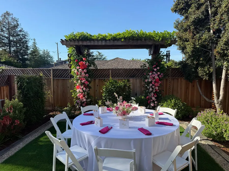 Rose arch curving over a garden round set in crisp white cloth with fuchsia napkins at each seat