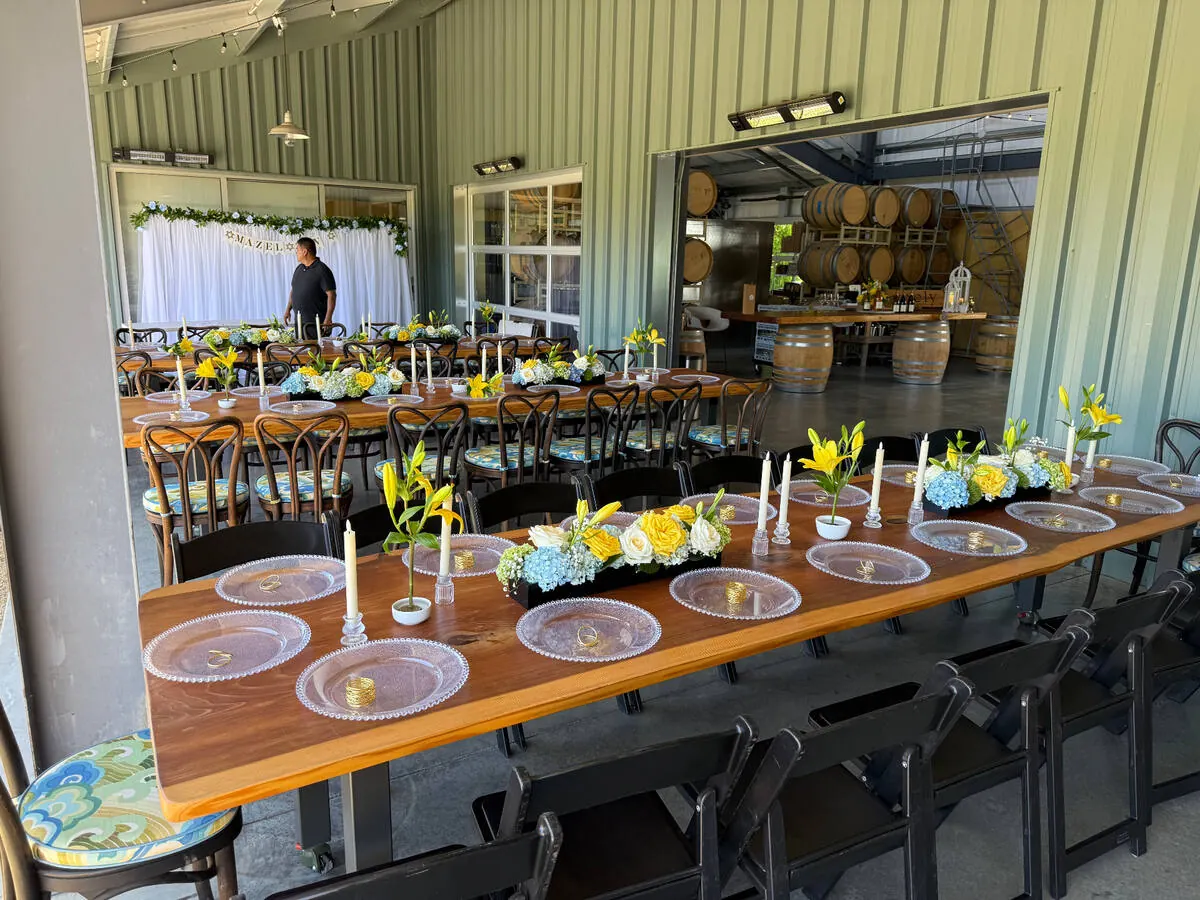 Long table carrying lily, hydrangea and rose arrangements between slim tapers down its length