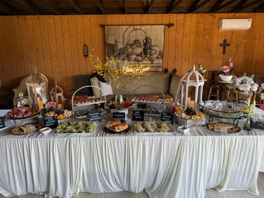 Grazing tablescape stacked with charcuterie, tea sandwiches, glazed tarts and chilled salads over layered linens