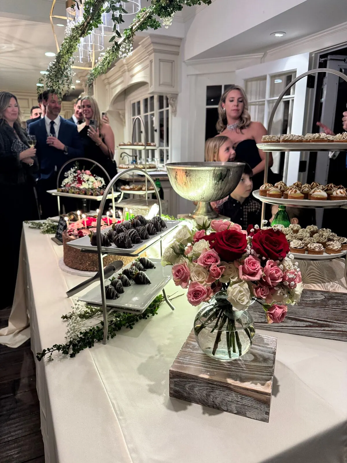 Reception sweets table with garden roses tucked between chocolate-dipped strawberries and small pastries